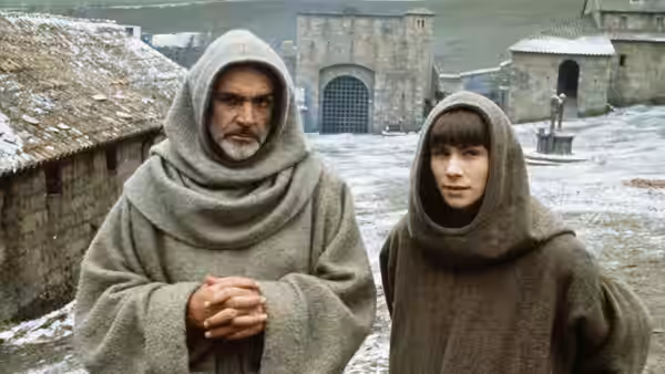 William of Baskerville (Sean Connery) and Adso of Melk (Christian Slater) stand in the snowy abbey courtyard