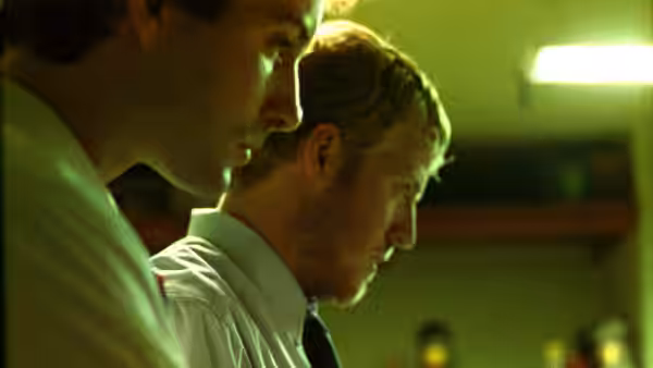 Aaron (Shane Carruth) standing beside another man in profile view