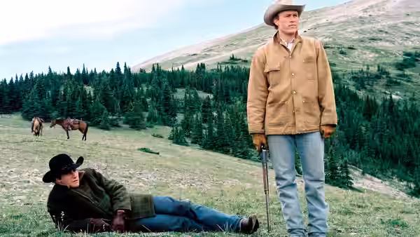 Jack Twist (Jake Gyllenhaal) reclining on the grass while Ennis Del Mar stands nearby