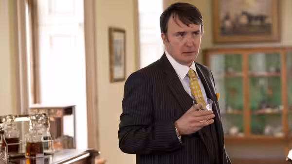 Man in pinstripe suit with yellow tie holding a whiskey glass