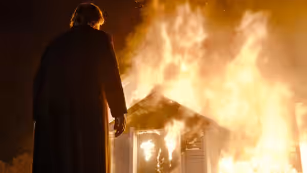 Father James (Brendan Gleeson) standing before a burning building at night
