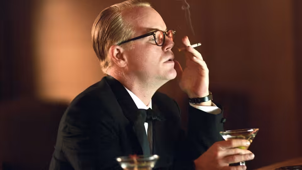 Truman Capote (Philip Seymour Hoffman) smoking a cigarette while holding a cocktail