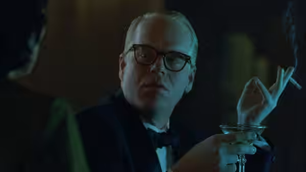 Truman Capote (Philip Seymour Hoffman) gesturing with a lit cigarette at a bar