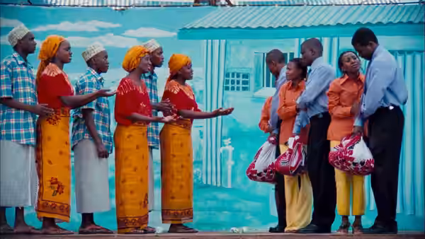 Group of men and women in colorful attire standing before a turquoise building