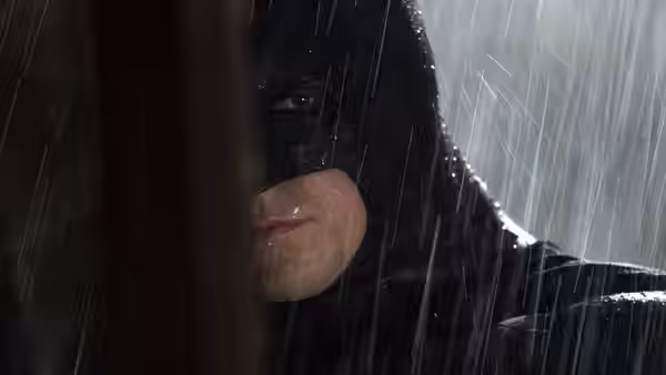 Batman standing in heavy rain with water running down his masked face