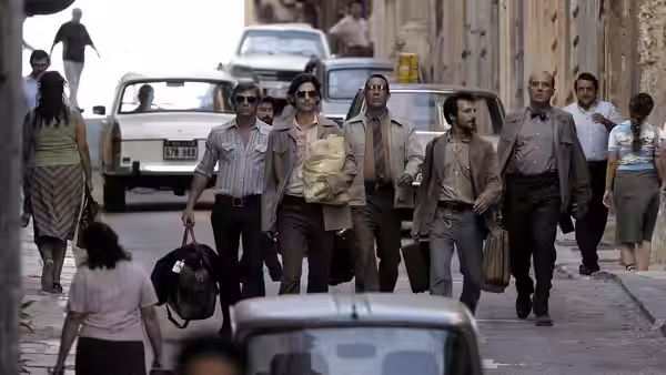 A group of men walk along a city street carrying bags and cases