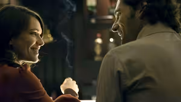 A smiling woman and man hold hands across a table in dim light
