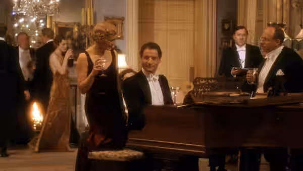 man seated at piano while woman stands nearby with a glass