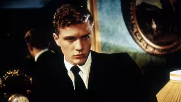 young man in black suit and tie looks ahead intently