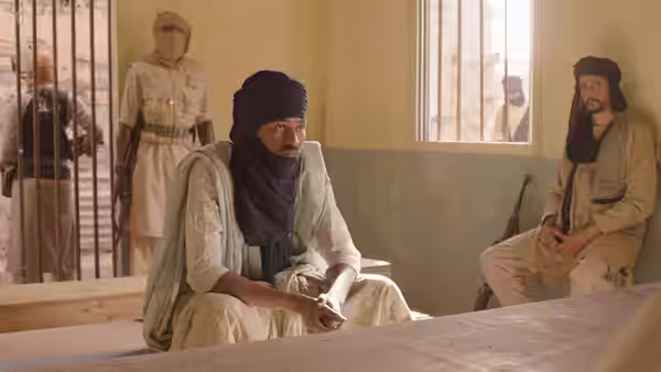 A turbaned man sits on the floor inside a room with barred windows