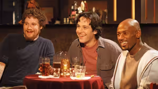Three men laugh and drink together at a table in a bar