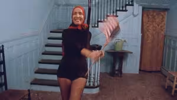 Woman in red headscarf holds a feather duster in a hallway