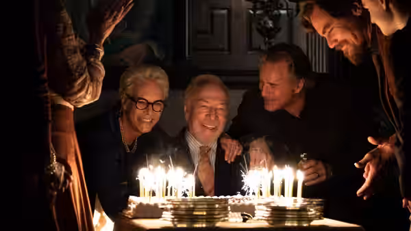 Harlan Thrombey laughing at his birthday cake surrounded by family