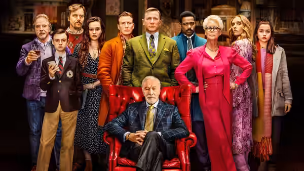 The cast assembled together with Benoit Blanc seated in a red chair