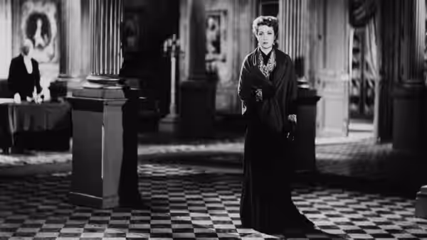 A woman in a long dark dress stands alone in a grand tiled hall