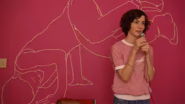 Christine (Miranda July) speaking into a microphone against a pink wall