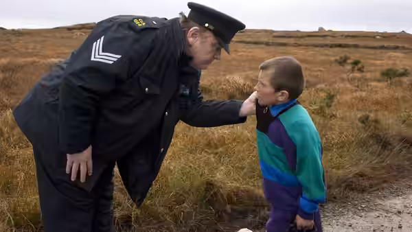 Police sergeant touching young boy's chin on rural moorland path