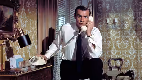 James Bond (Sean Connery) speaking on the telephone while seated at a desk