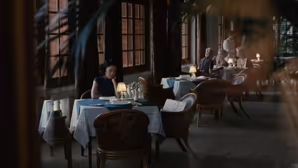 Wong Chia Chi (Tang Wei) sits alone at a restaurant table as diners gather behind her