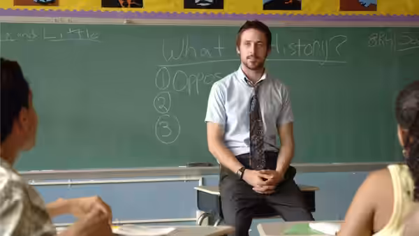 Dan Dunne (Ryan Gosling) seated before a chalkboard in a classroom with students