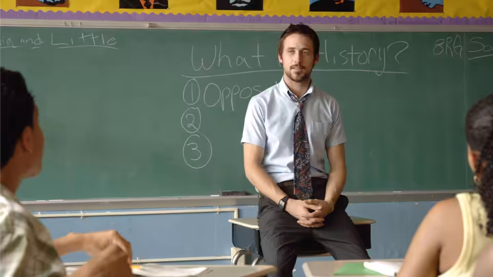 Dan Dunne (Ryan Gosling) seated before a chalkboard in a classroom with students