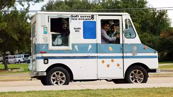 Two men inside an ice cream truck parked on a suburban street