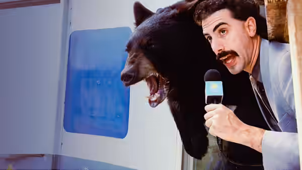 Borat (Sacha Baron Cohen) holding a microphone beside a bear with open mouth