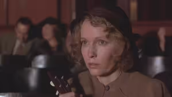 Cecilia (Mia Farrow) seated in a theater holding her gloves with a concerned expression