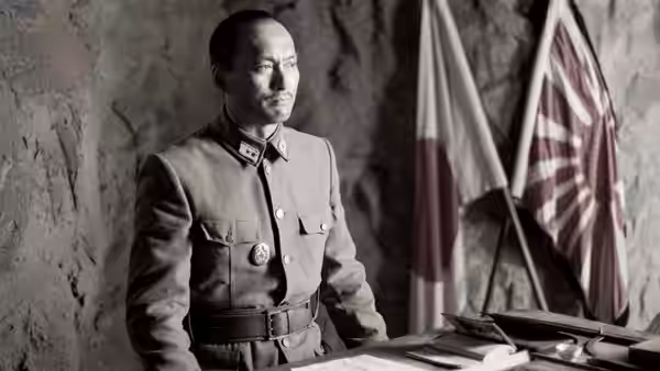 General Tadamichi Kuribayashi seated at a desk with flags behind