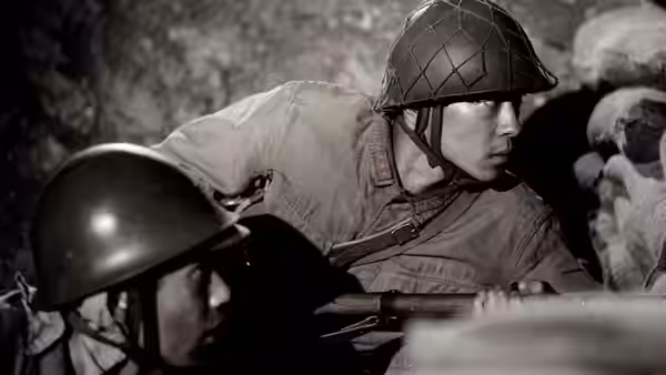 Two soldiers in helmets looking over sandbags in a trench