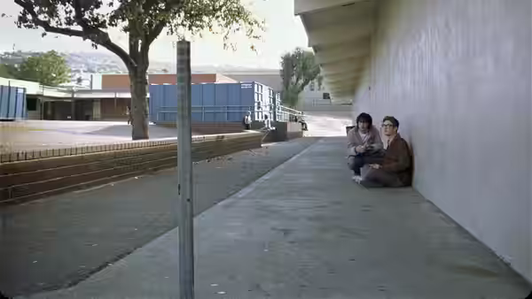 Two young men sitting on the ground beside a school building