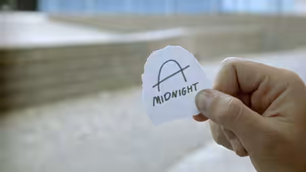 A hand holding a torn note reading A MIDNIGHT