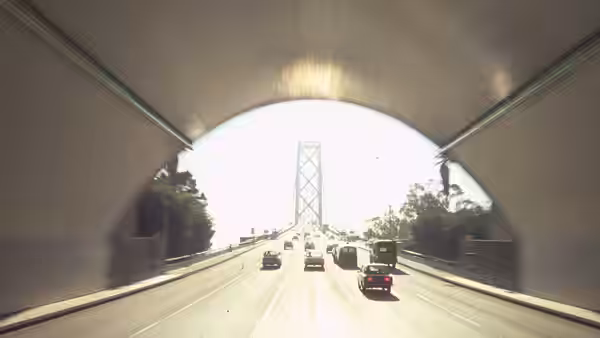 cars traveling on highway through tunnel toward distant suspension bridge