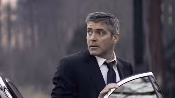 Michael Clayton (George Clooney) stands holding an open car door outdoors at dusk