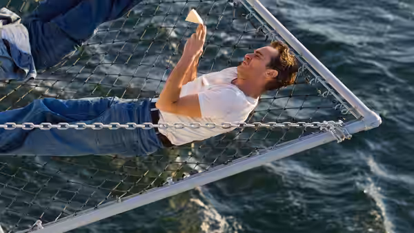 Freddie Quell (Joaquin Phoenix) clings to a cargo net above the ocean holding paper