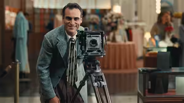 Freddie Quell (Joaquin Phoenix) leans against a large format camera on a tripod