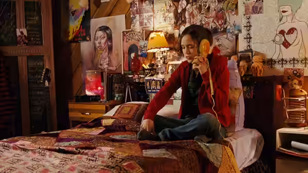 Juno (Elliot Page) listening to music on headphones while seated on her bed