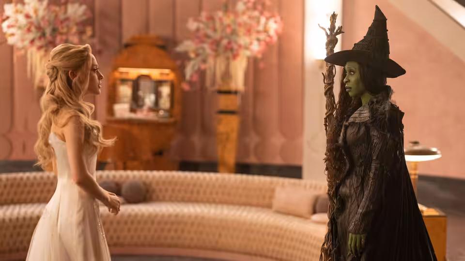 Glinda (Ariana Grande) facing Elphaba (Cynthia Erivo) in a pink lounge