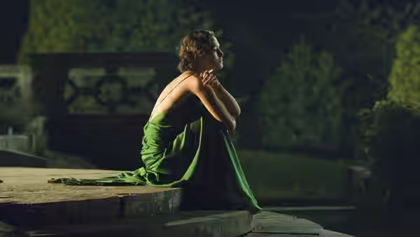 Cecilia Tallis (Keira Knightley) in a green dress sitting on steps at night