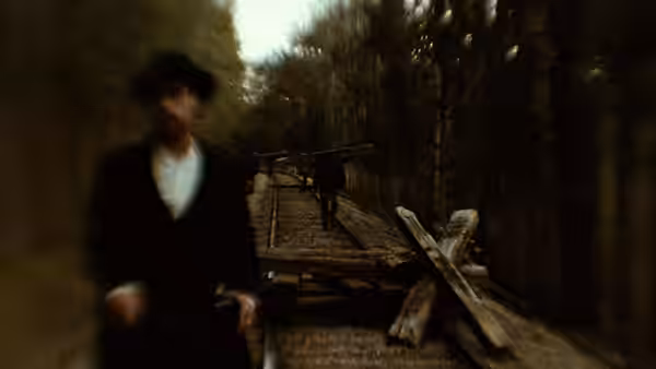 Man in dark coat on wooden railway tracks with figure ahead