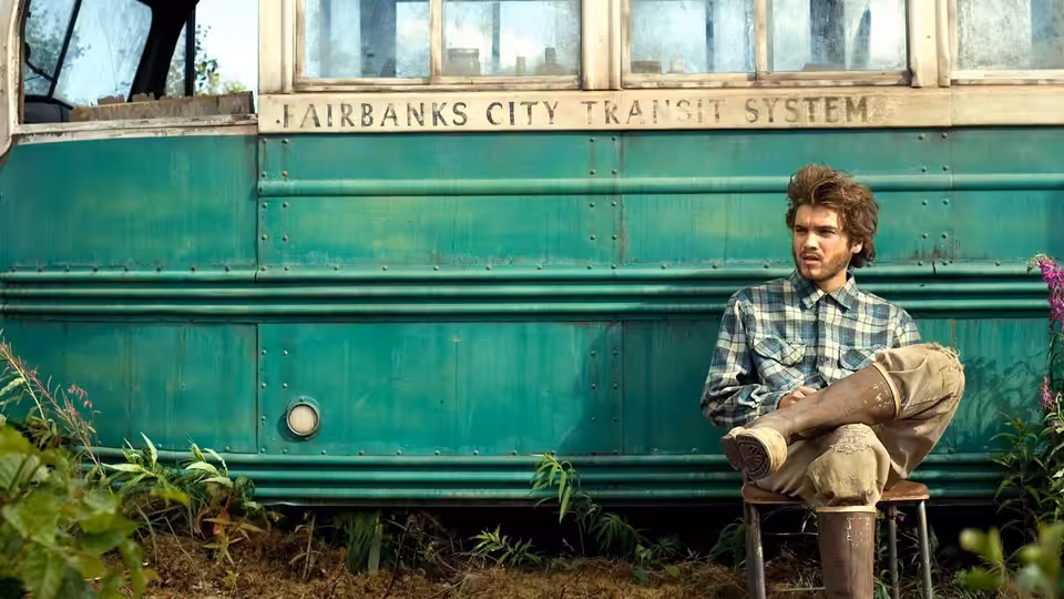 Christopher McCandless (Emile Hirsch) sitting on a stool beside the green bus