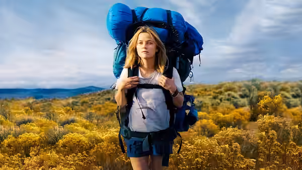 Cheryl Strayed (Reese Witherspoon) pausing amid yellow wildflowers with backpack
