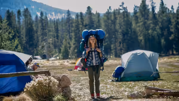 Cheryl Strayed (Reese Witherspoon) standing among tents in a grassy clearing