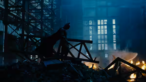 Batman (Christian Bale) standing amid rubble in a burning building
