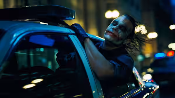 Joker (Heath Ledger) leaning from a police car on a city street at night