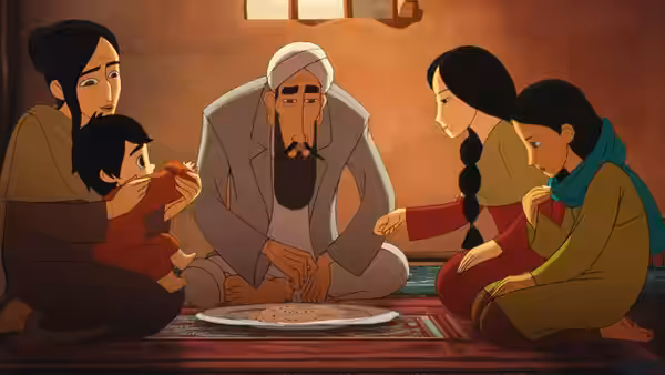 A bearded man in a turban sits with his family around a shared plate on the floor