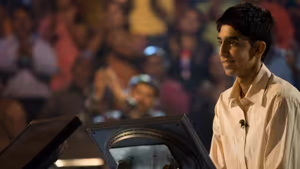 Jamal (Dev Patel) smiles while standing at a game show podium
