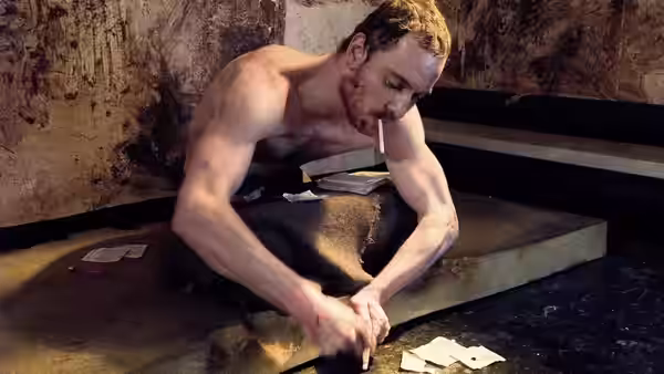 Bobby Sands (Michael Fassbender) sits on steps smoking in a grimy room