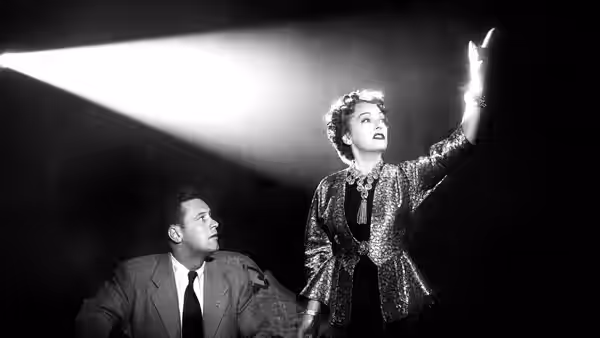 Norma Desmond (Gloria Swanson) gestures upward beside Joe Gillis (William Holden)