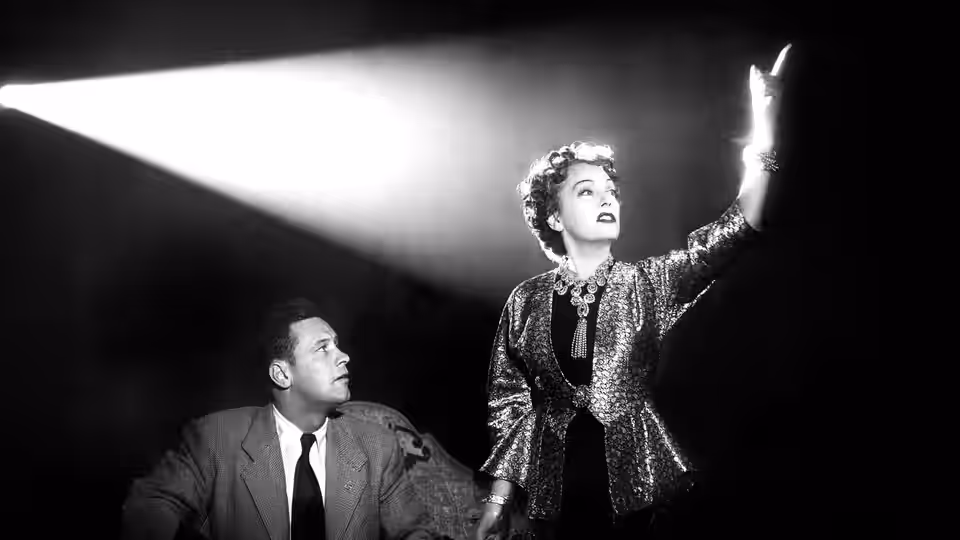 Norma Desmond (Gloria Swanson) gestures upward beside Joe Gillis (William Holden)